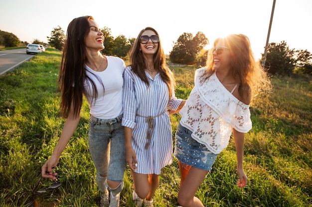 Mooie jonge vrouwen in zonnebril gekleed in de mooie kleren staan in het veld en glimlachen op een zonnige dag. .