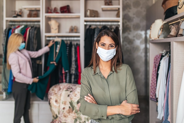 Mooie jonge vrouwen met beschermende gezichtsmaskers die elegante kleding proberen in een dure boetiek of winkel.