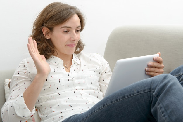 Mooie jonge vrouwenvrouw met een tablet in de bank