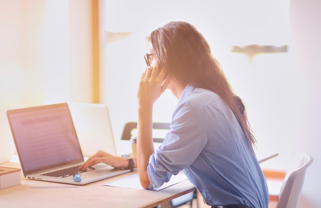 Mooie jonge zakenvrouw die aan een bureau zit en op een mobiele telefoon praat