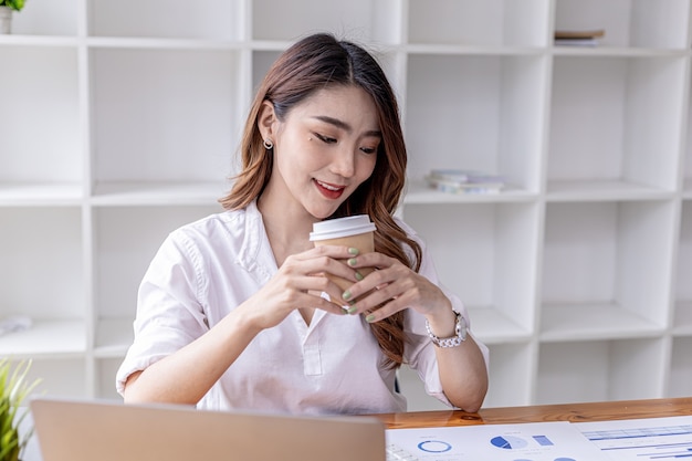 Mooie jonge zakenvrouw die hete koffie drinkt. Een zakenvrouw drinkt overdag koffie, ze controleert documenten van de financiële afdeling. Aziatische zakenvrouw concept.