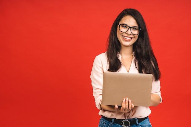 Mooie jonge zakenvrouw in casual bedrijf laptop op kantoor geïsoleerd op rode achtergrond Werken met computer