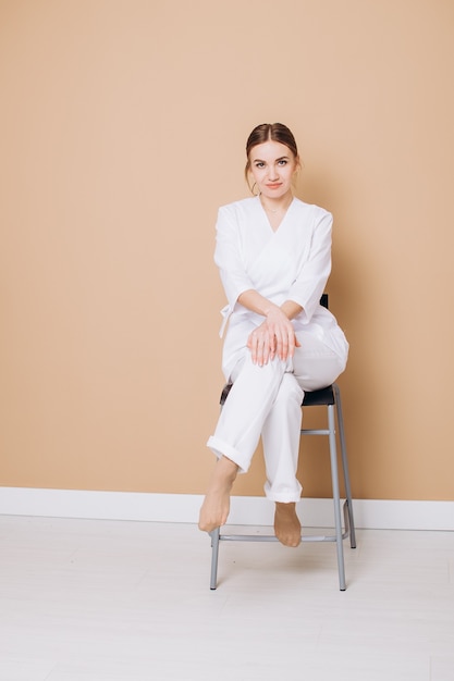 mooie jonge zakenvrouw in een wit pak zit op een stoel tegen een bruine achtergrond