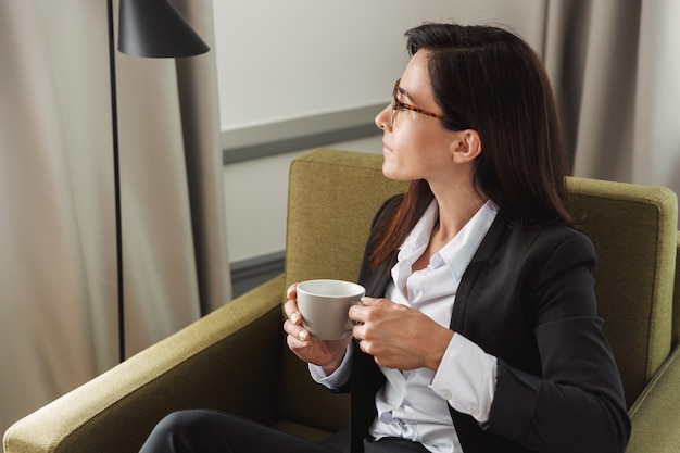 mooie jonge zakenvrouw in formele kleding binnenshuis thuis koffie drinken.