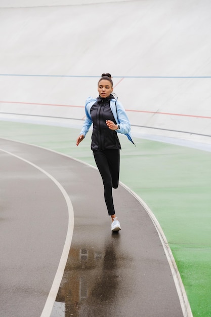 Mooie jonge, zelfverzekerde afrikaanse sportvrouw die in het stadion loopt