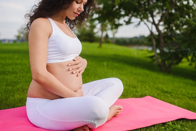 Mooie jonge zwangere vrouw die yoga in park doet. de zwangere vrouw met overhandigt buik.