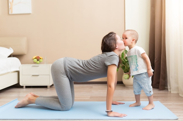 Mooie jonge zwangere vrouw en kleine jongen die lacht terwijl hij op yogamat ligt