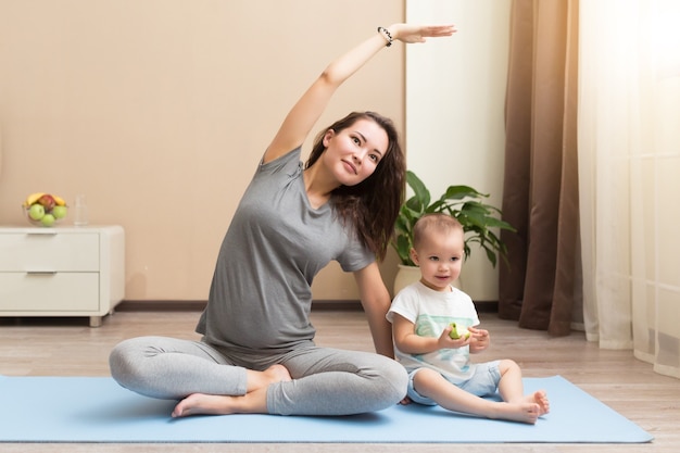 Mooie jonge zwangere vrouw en kleine jongen die lacht terwijl hij op yogamat ligt