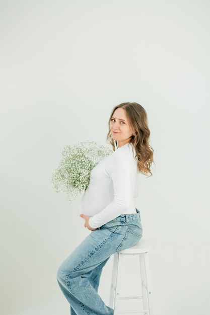 Foto mooie jonge zwangere vrouw met een boeket voorjaarsbloemen op een witte achtergrond