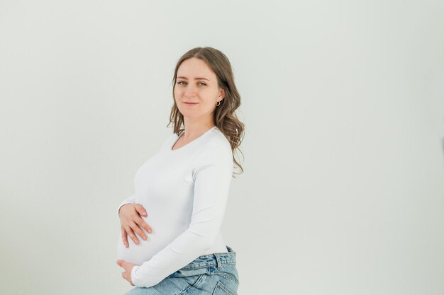 Mooie jonge zwangere vrouw op witte achtergrond Stijlvol model met buik in een wit bodysuit