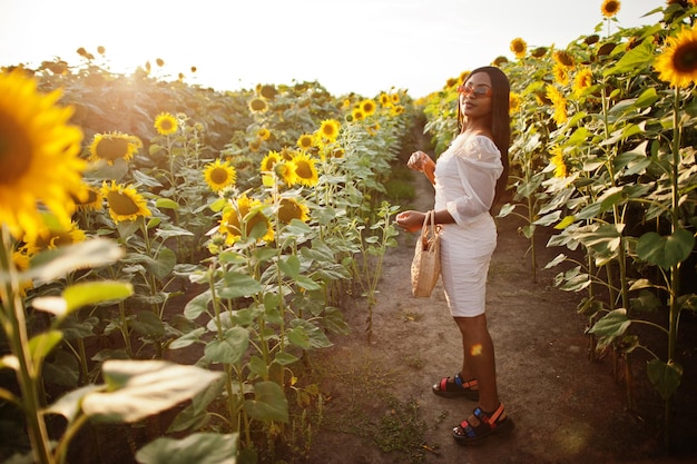 Mooie jonge zwarte vrouw draagt zomerjurk pose in een zonnebloemveld