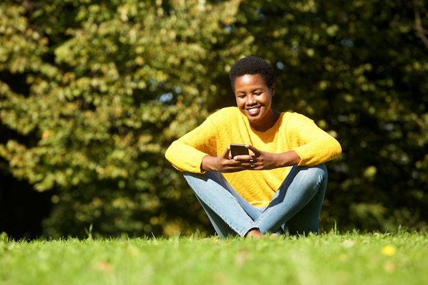 mooie jonge zwarte vrouw zit in het park en kijkt naar mobiele telefoon