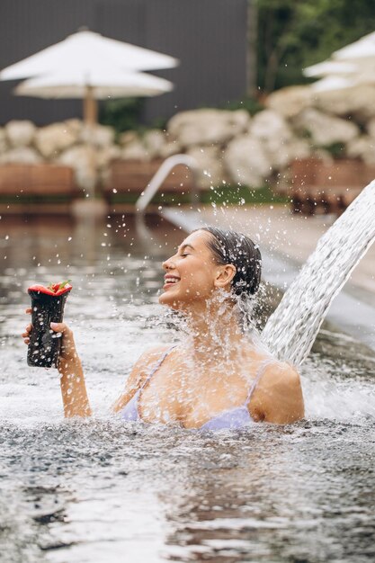 Mooie jongedame in bikini cocktail drinken krijgen hydrotherapie in buitenzwembad