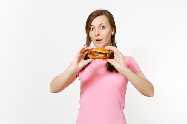 Mooie jongedame in roze t-shirt met vlechten in handen hamburger geïsoleerd op een witte achtergrond. Goede voeding of Amerikaans klassiek fastfood. Kopieer ruimte voor advertentie. Reclame gebied.