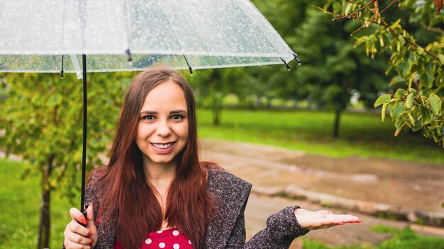 Mooie jongedame permanent met transparante paraplu in regen op straat