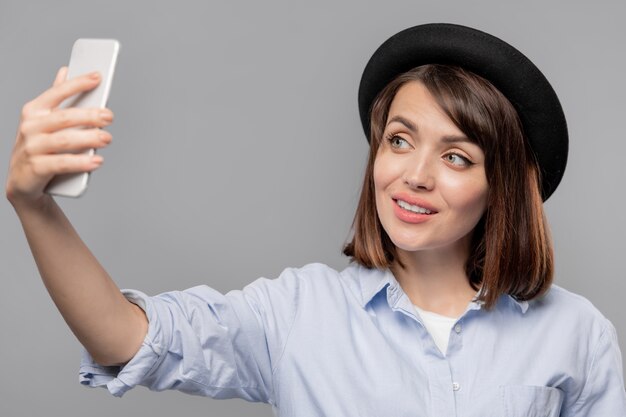 Mooie jongedame smartphone kijken terwijl het maken van selfie geïsoleerd