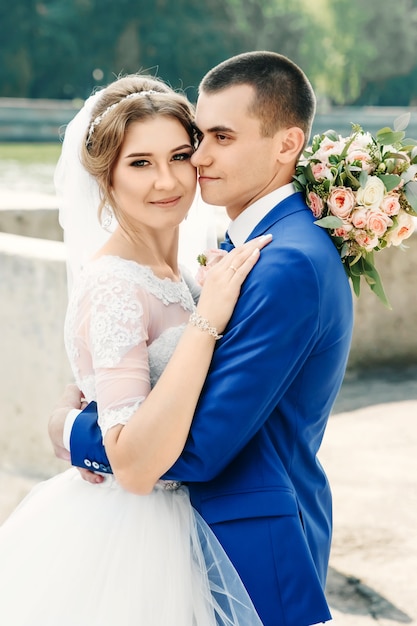 Mooie jongen en meisje, bruid in een witte trouwjurk, bruidegom in een klassiek blauw pak tegen een achtergrond van de natuur. Bruiloft, familiecreatie.