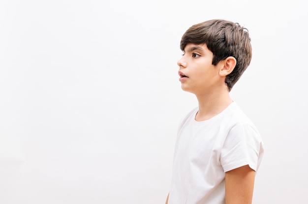 Mooie jongen jongen draagt casual t-shirt staande over geïsoleerde witte achtergrond op zoek naar kant.