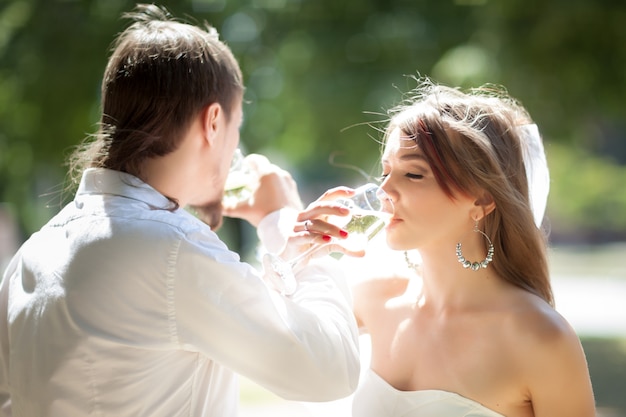 Mooie jonggehuwden drinken champagne buitenshuis.