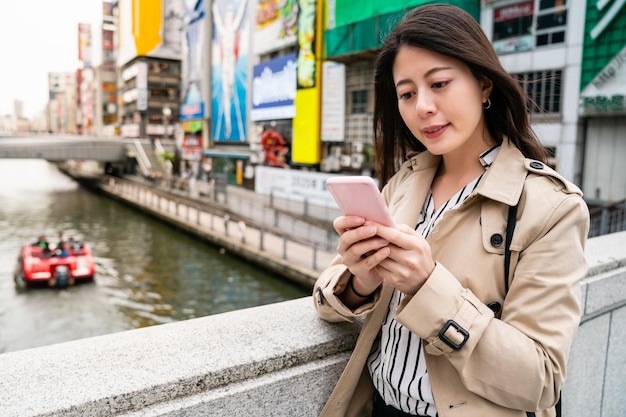 mooie kantoordame die op de brug staat en mobiele telefoon gebruikt om de e-mail te controleren