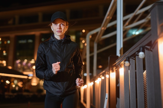 Mooie kaukasische roodharige fitness vrouw in zwarte atletische kleding jogt op stadsstraat vertrouw...