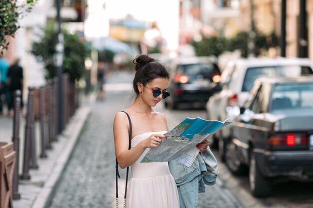 Mooie Kaukasische toeristenvrouw die de kaart op de straat van de stad bekijken