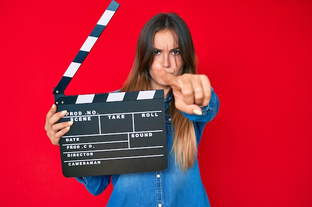 Mooie kaukasische vrouw met videofilm duig wijzend met de vinger naar de camera en naar jou, zelfverzekerd gebaar dat er serieus uitziet