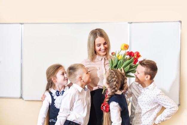 Mooie kinderen-studenten samen in de klas op school geven bloemen aan hun beste vrouwelijke leraar