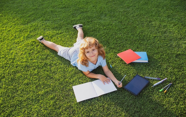 Mooie kindjongen die op notitieboekje op grasachtergrond schrijft die kinderen boek in parkconcept kid lezen