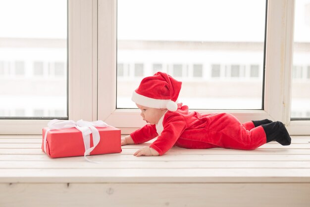 Mooie kleine baby viert Kerstmis. Nieuwjaarsvakantie. Baby in een kerstkostuum en in een kerstmuts.