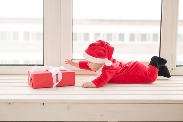 Mooie kleine baby viert Kerstmis. Nieuwjaarsvakantie. Baby in een kerstkostuum en in een kerstmuts.