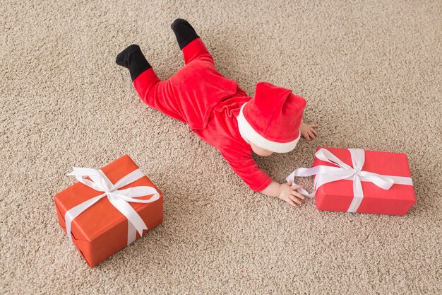 Mooie kleine baby viert Kerstmis. Nieuwjaarsvakantie. Baby in een kerstkostuum en in kerstmuts en geschenkdoos, bovenaanzicht.