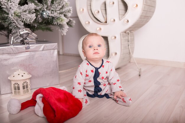 Mooie kleine baby viert Kerstmis. Nieuwjaarsvakantie. Baby in kerstkostuum met cadeau