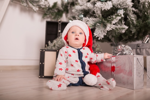 Mooie kleine baby viert Kerstmis. Nieuwjaarsvakantie. Baby in kerstkostuum met cadeau