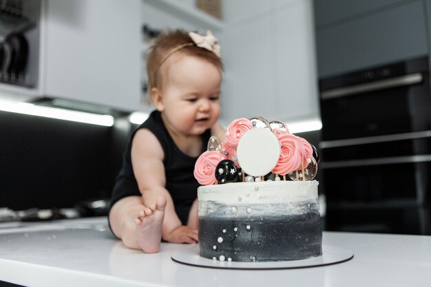 Mooie kleine babymeisje zit aan tafel met een verjaardagstaart in de keuken