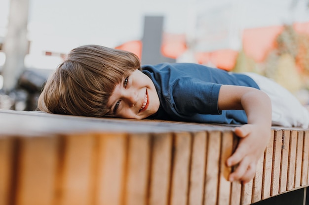 Mooie kleine brunette jongen in een blauw T-shirt en witte korte broek ligt op een houten bankje in het park. kind zonnebaadt en neemt een luchtbad buiten. begrip gezondheid. ruimte voor tekst. Hoge kwaliteit foto