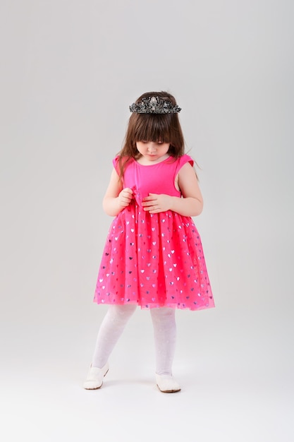 Mooie kleine brunette meisje in roze prinses jurk met een kroon op een grijze achtergrond. schattige baby