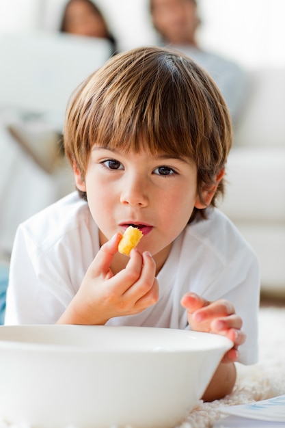 Mooie kleine jongen die spaanders eet die op de vloer liggen