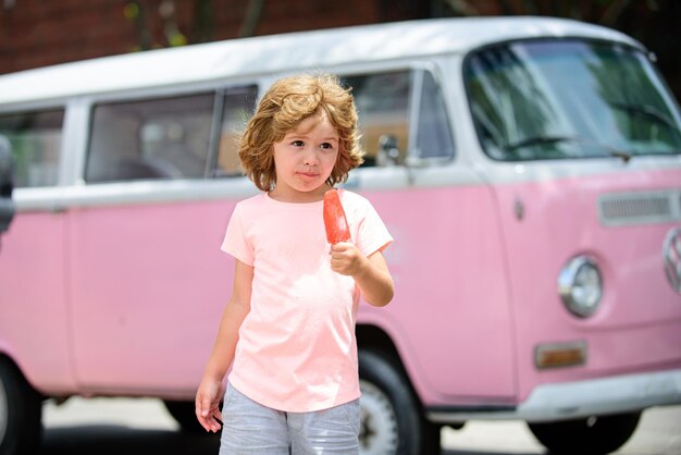 Mooie kleine jongen in een roze jurk die een ijsje eet