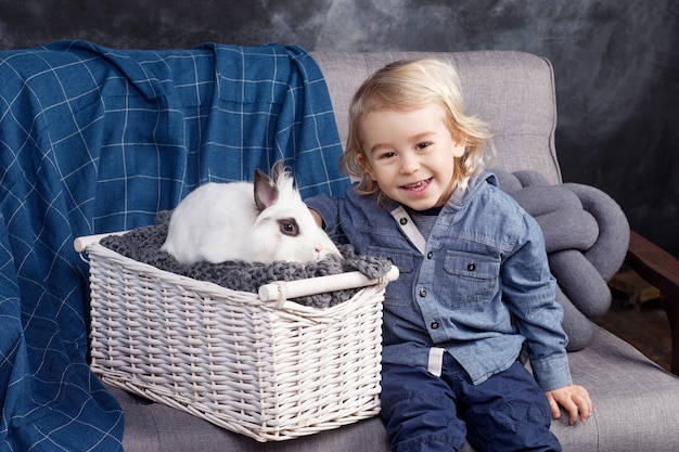 Mooie kleine jongen speelt met een wit konijn. De jongen lacht, een blik in de camera