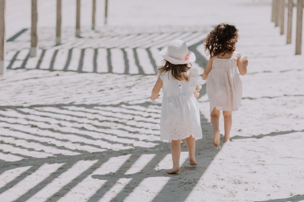 Mooie kleine meisjes in witte jurk en hoed die ijs eten op het strand in de zomer