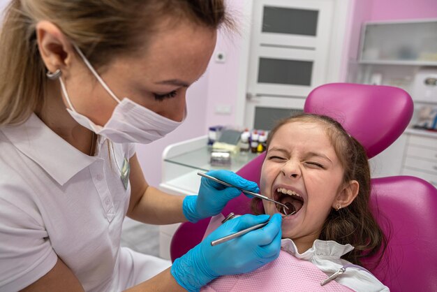 Mooie kleine vrouwelijke patiënt grimassen tijdens mondeling onderzoek door vrouwelijke tandarts