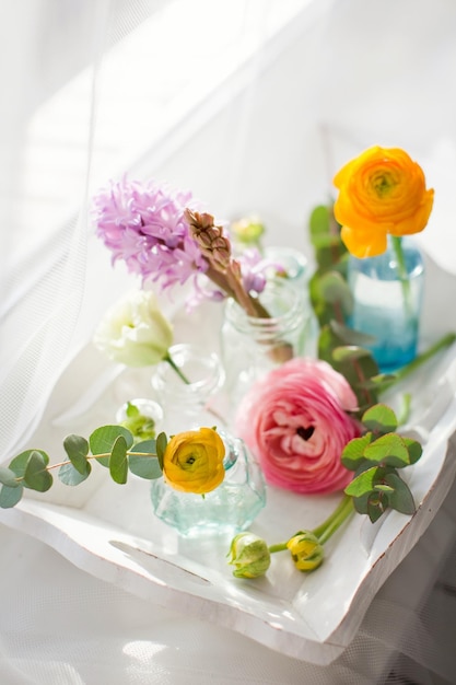 Mooie kleurrijke bloemen in glazen flessen op een vintage houten dienblad Bloemen bij zonlicht