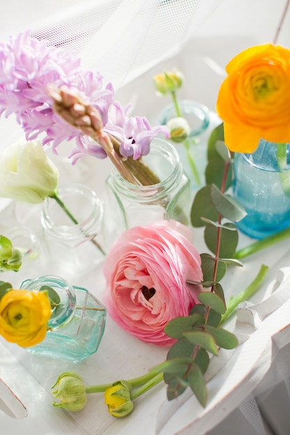 Mooie kleurrijke bloemen in glazen flessen op een vintage houten dienblad Bloemen bij zonlicht