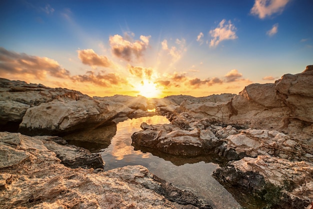 Mooie kleurrijke zonsondergang in de buurt van de zee op Cyprus met dramatische wolken en rotsblokken Reflecties in het water Schoonheidswereld natuurlijke buiten reizen achtergrond