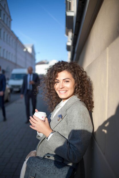 mooie krullende jonge vrouw in de stad met een kopje koffie