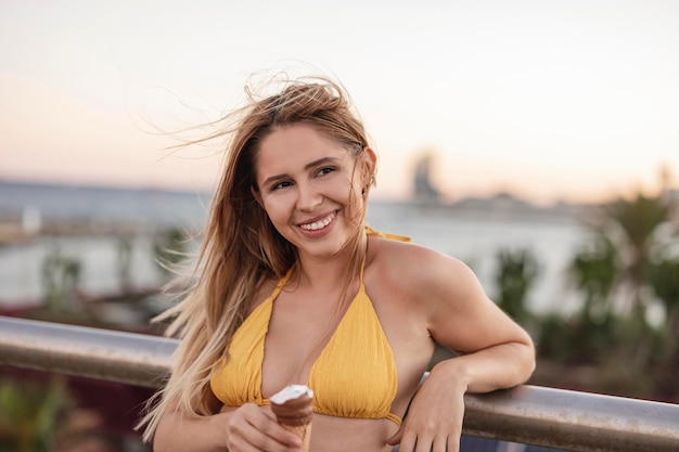 Mooie lachende blanke vrouw die ijs eet op het strand in bikini