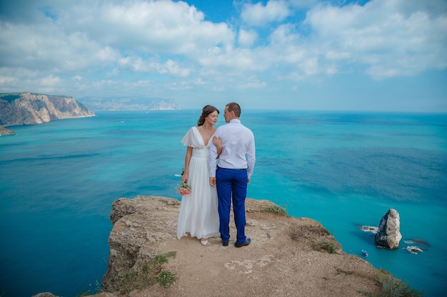 Mooie lachende jonge bruid en bruidegom wandelen op het strand zoenen en plezier hebben huwelijksceremonie in de buurt van de rotsen en de zee Huwelijksceremonie aan de kust van Cyprus