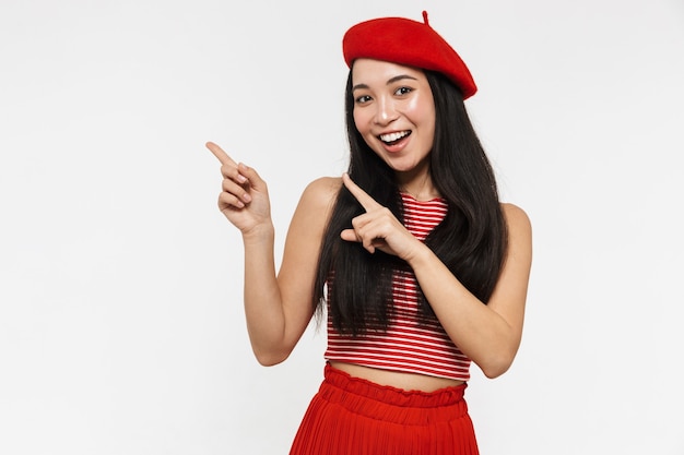 mooie lachende jonge mooie Aziatische vrouw poseren geïsoleerd over witte muur wijzen.