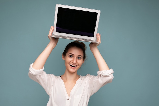 Mooie lachende jonge vrouw met netbook computer kijken naar camera met wit overhemd geïsoleerd op blauwe achtergrond